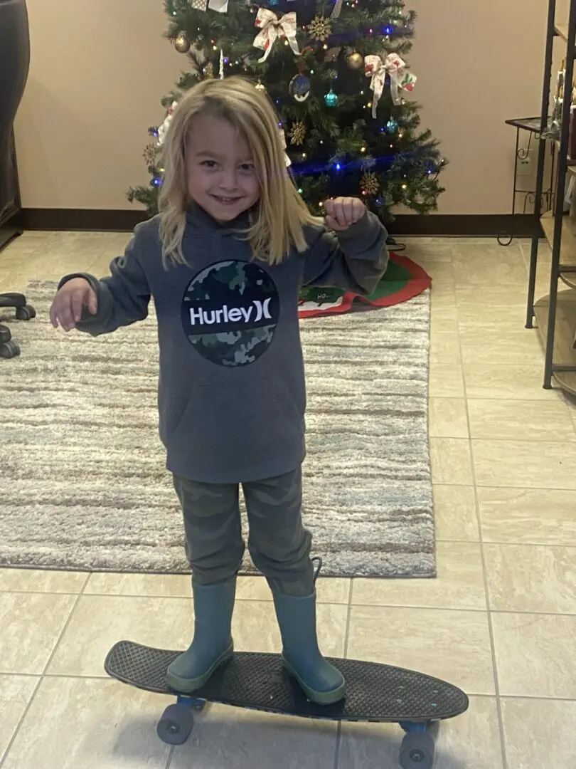 A small girl standing on a skate board with a christmas tree in the back