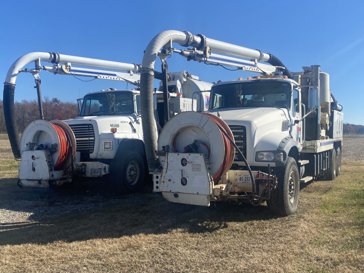 Two large trucks parked in a field with pipes attached to the back of them.